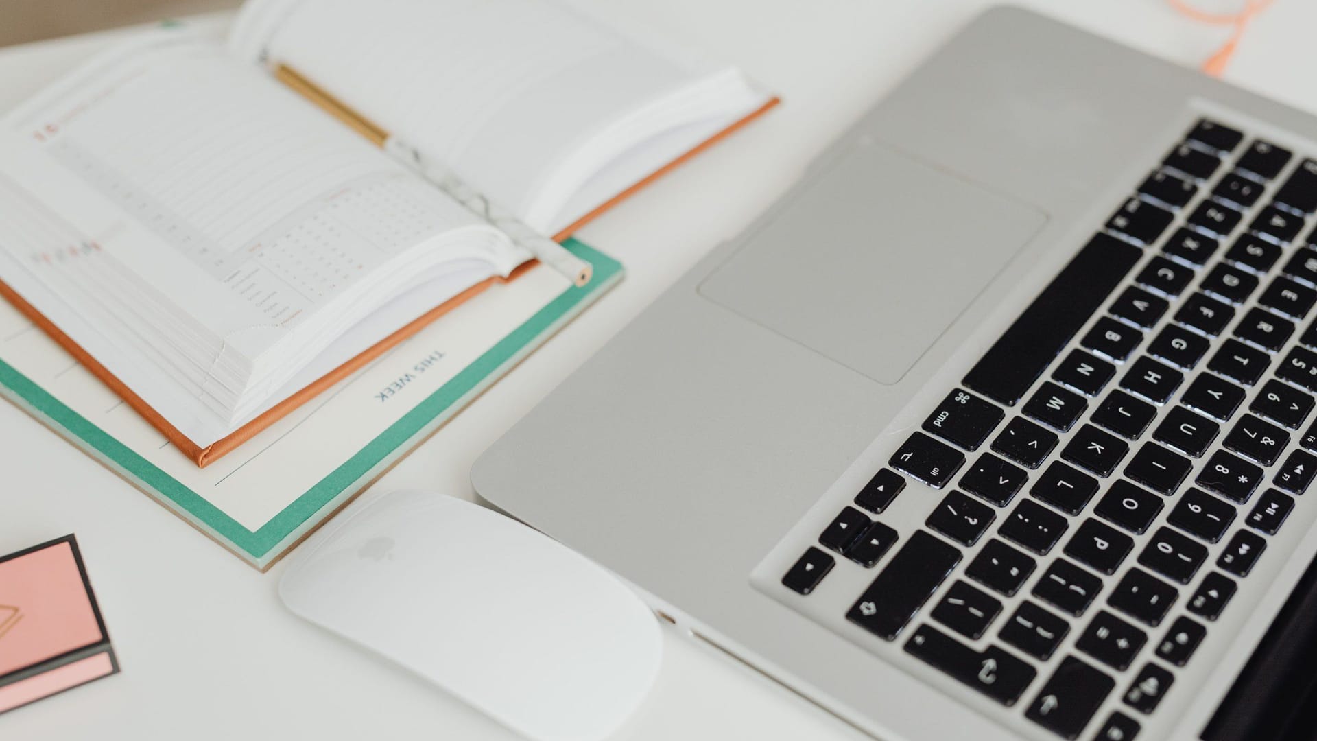 An open weekly planner on a white desk beside a silver laptop and a white mouse.