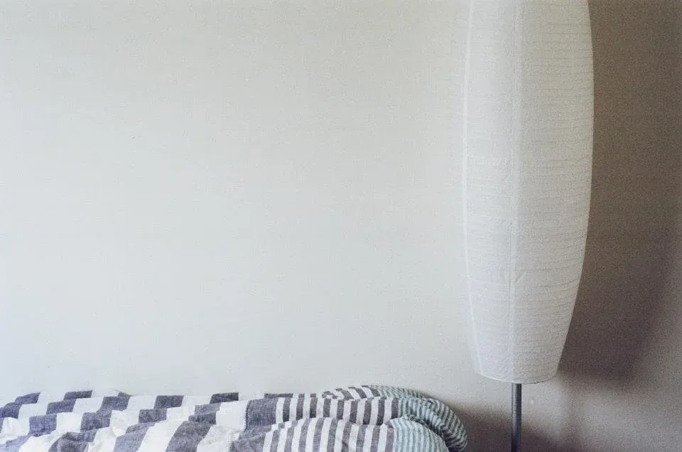 A tidy guest bedroom with fresh white and striped bedding and a bedside lamp, illustrating the kind of bedding and mattress area a host or inspector checks after a bed bug report.