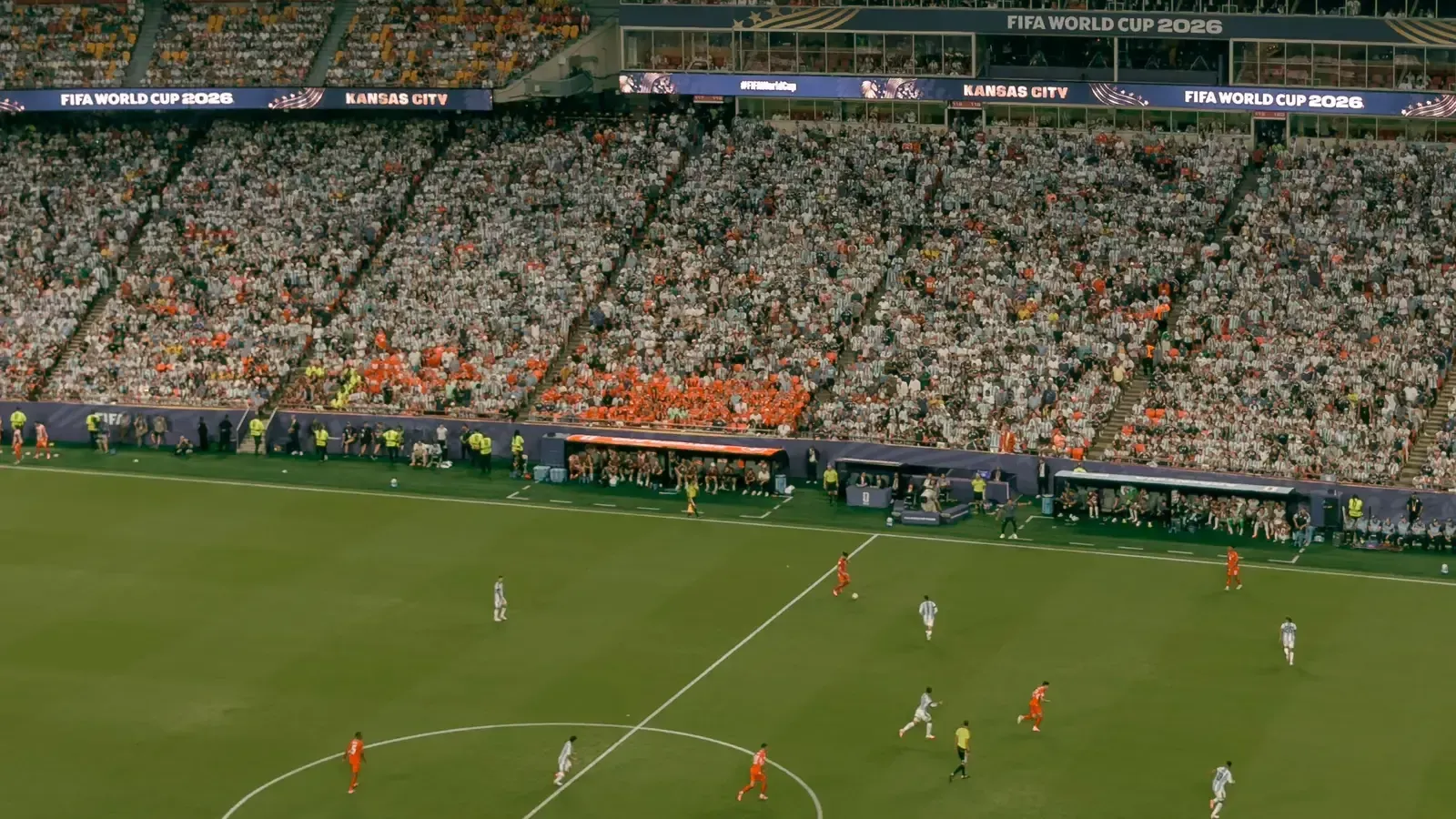 A packed stadium during a 2026 FIFA World Cup match in Kansas City, with orange-shirted and white-shirted fans in the stands and players on the pitch.